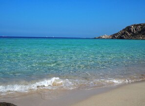 A beach with clear turquoise water, gentle waves, and a rocky outcrop in the background. - Enjoy tranquility in a comfortable villa with 140 m² and two hectares of private garden  (Bassacutena)