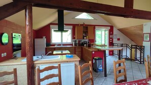 Cocina compacta con horno integrado, un lavabo y una ventana. En la zona de comedor, hay sillas de madera y una mesa.