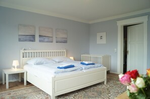 Cozy retreat with a comfortable white bed, two nightstands, and a crib, set against a light blue wall adorned with artwork.