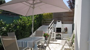 Patio esterno con tavolo e sedie, un barbecue e una pianta in vaso.
