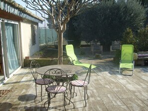 An outdoor patio with a round table and four chairs, surrounded by a low stone wall and a tree. - charming cottage in the heart of Provence (Saint-Andiol)