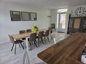 Een eethoek met een houten tafel en stoelen, een bloevas en een grote wandklok.