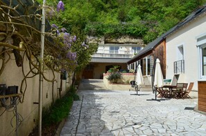 A stone-paved courtyard with a wooden fence, outdoor seating, and a view of a building with a balcony.