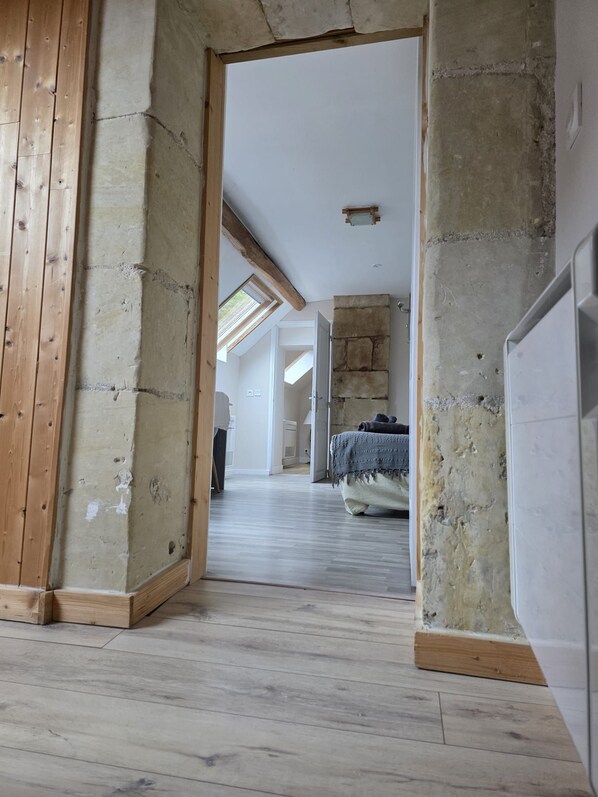 A room with a sloped ceiling, wooden beams, a stone wall, and a bed with a blanket.