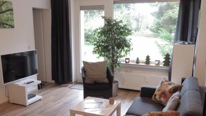Una sala de estar con un televisor de pantalla plana, un sofá, una mesa de centro y una planta en maceta.