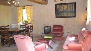 Un área de comedor con una mesa y sillas de madera, un televisor sobre un mueble bajo y un sofá.
