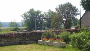 Paisaje rural con un muro de piedra, una pérgola de madera y diversas plantas y flores.