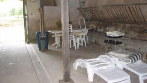 Un área de estar al aire libre rústica con sillas y mesas de plástico, suelo de concreto y pared de piedra.
