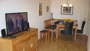 A living room with a television on a wooden cabinet, a dining table with chairs, and a chandelier. -  Bright and friendly apartment in the center of Grömit (Grömitz)