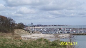 A marina with numerous boats docked, a sandy beach area, and a construction site in the background. -  Bright and friendly apartment in the center of Grömit (Grömitz)