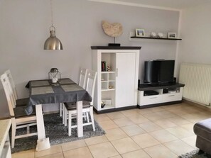 Un espace de vie compact comprenant une table à manger, des chaises, un téléviseur et une bibliothèque.