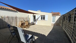 Um pátio com mesa e cadeiras, cerca de madeira e um edifício com telhado de telhas.