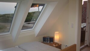 Ett sovrum med ett sluttande tak, takfönster, ett sängbord med en lampa och en säng.
