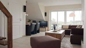 Ett modernt vardagsrum med matplats, TV och en balkong med utsikt.