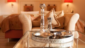 A hotel room with a glass coffee table, two decorative silver candle holders, and a bed with a beige and brown color scheme.