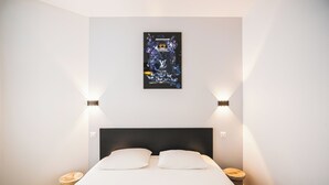 Un lit bien fait, avec du linge de lit blanc et deux oreillers, une tête de lit noire et une œuvre d’art accrochée au mur au-dessus.