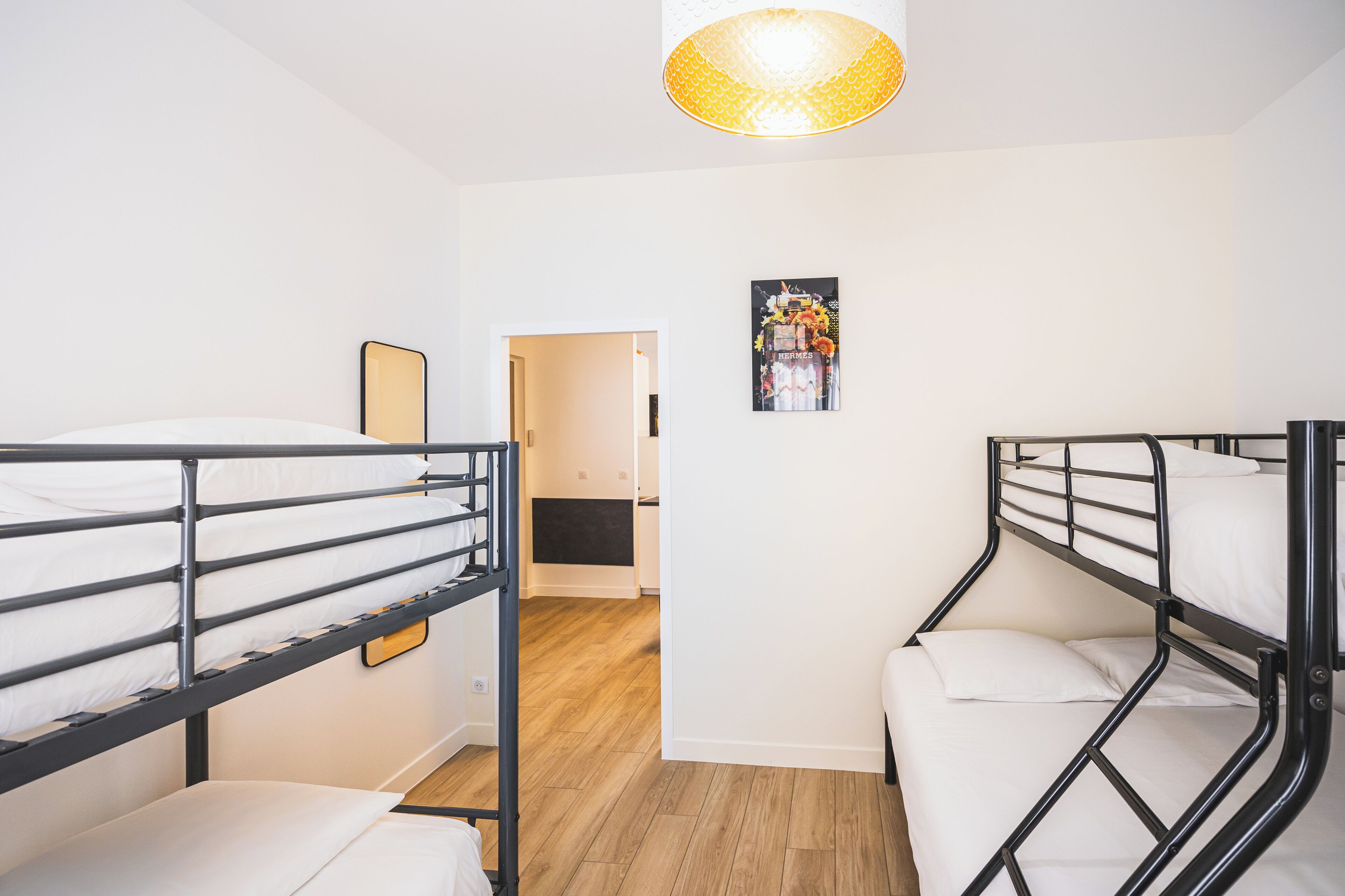 Ein Schlafsaalzimmer mit Etagenbetten, Holzboden, kleinem Schreibtisch und einer Wandlampe.