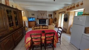 A dining area with a red tablecloth, wooden chairs, a television, a fireplace, and a refrigerator. - House in the countryside, with large expanses of woods and fields. (Goujounac)