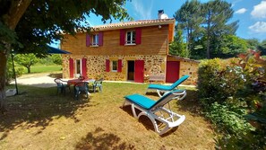 A stone house with red shutters, a patio with chairs, and a lawn. - House in the countryside, with large expanses of woods and fields. (Goujounac)