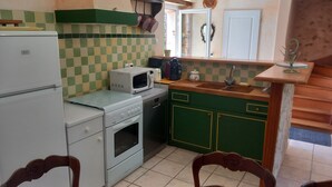 A compact kitchen with a refrigerator, microwave, stove, and sink. - House in the countryside, with large expanses of woods and fields. (Goujounac)
