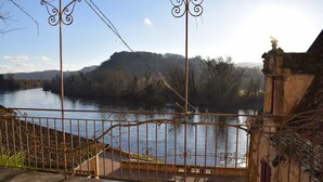 A river with a metal fence and a stone building in the background. - Charming rooms with view  (La Roque-Gageac)