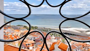 A view through ornate metal grilles, featuring a coastal cityscape with red-roofed buildings and a bridge in the distance. - Exclusive gallery apartment overlooking the golf course / beach (Charneca de Caparica)