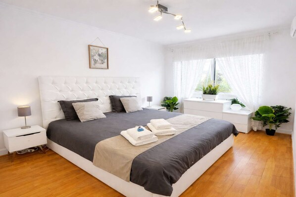 A modern bedroom with a large bed, bedside tables, a window with sheer curtains, and a ceiling light fixture.