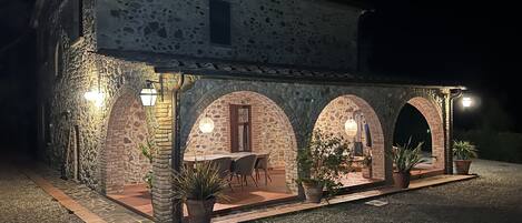 A stone building with a covered patio, potted plants, and outdoor seating.