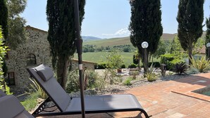 Un patio con poltrone relax e un tavolo, circondato da un muro in pietra e affaccio su un paesaggio verdeggiante.