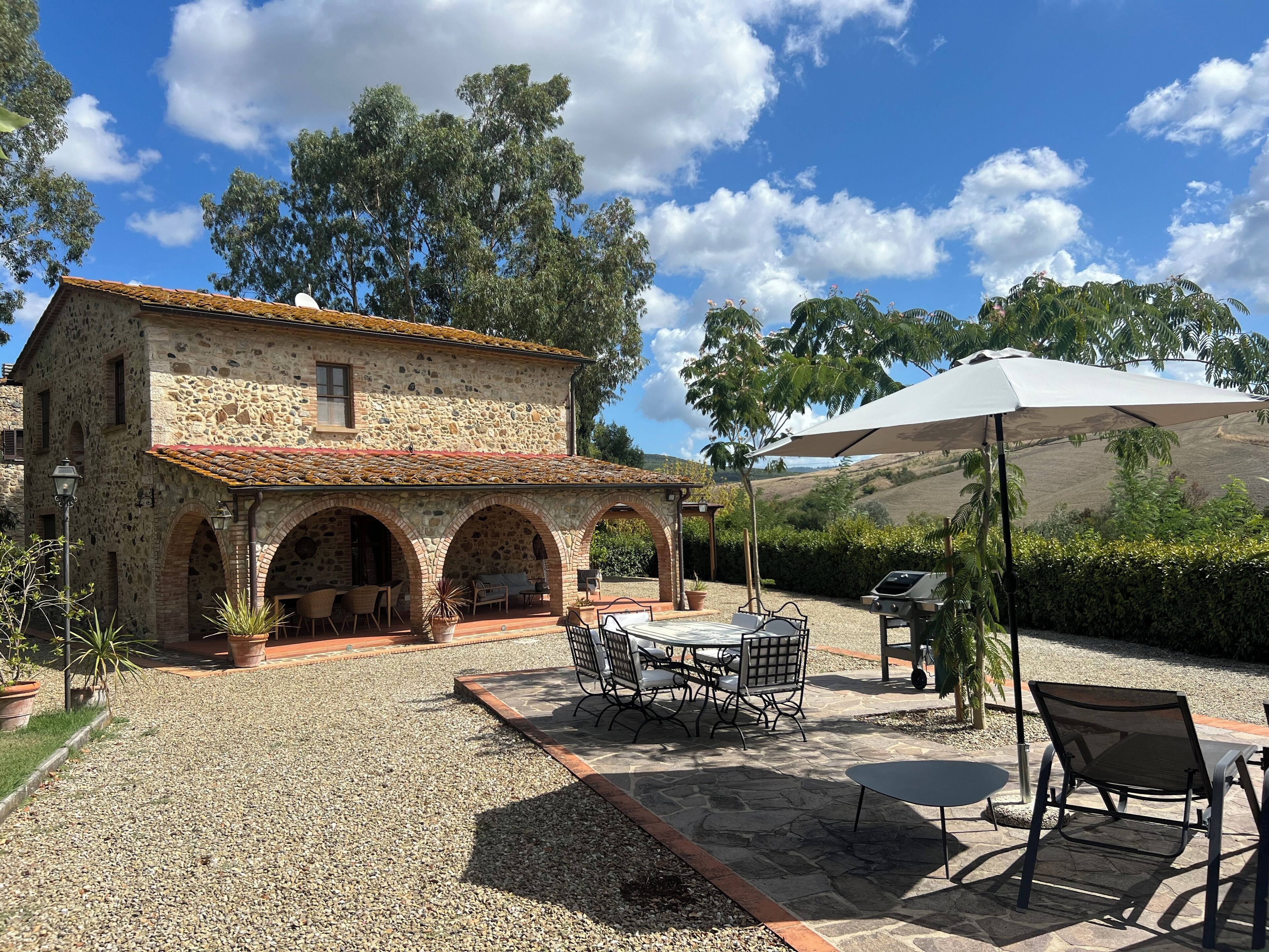 A stone building with a tiled roof, outdoor seating area with tables and chairs, and a grill.