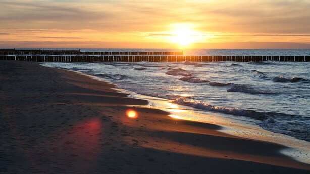 A beach with a wooden pier extending into the water during sunset.