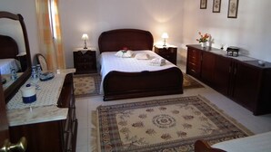 Une chambre à coucher comprenant un lit, des tables de chevet, une commode, un miroir, un bureau et un luminaire suspendu.