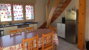 A kitchen with a dining table, chairs, a refrigerator, and a wooden staircase.