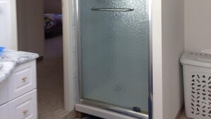 A narrow, glass-enclosed bathroom with a white sink and a trash bin.