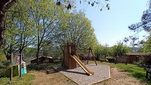 Une aire de jeux avec un toboggan et des structures d’escalade, entourée d’arbres et d’une zone recouverte de gravier.
