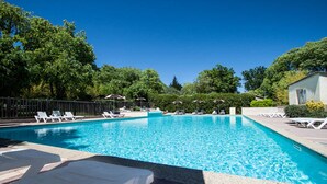 Une piscine entourée d’arbres et d’un petit bâtiment, avec des chaises longues et des parasols à proximité.