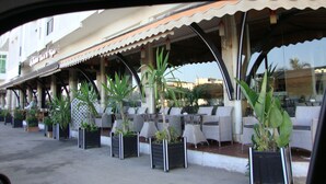 An outdoor seating area with tables and chairs, potted plants, and a building with a tiled roof in the background.