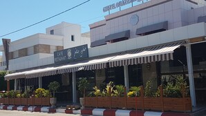 A cafe restaurant with a modern design, featuring a striped awning and wooden planters with yellow flowers.