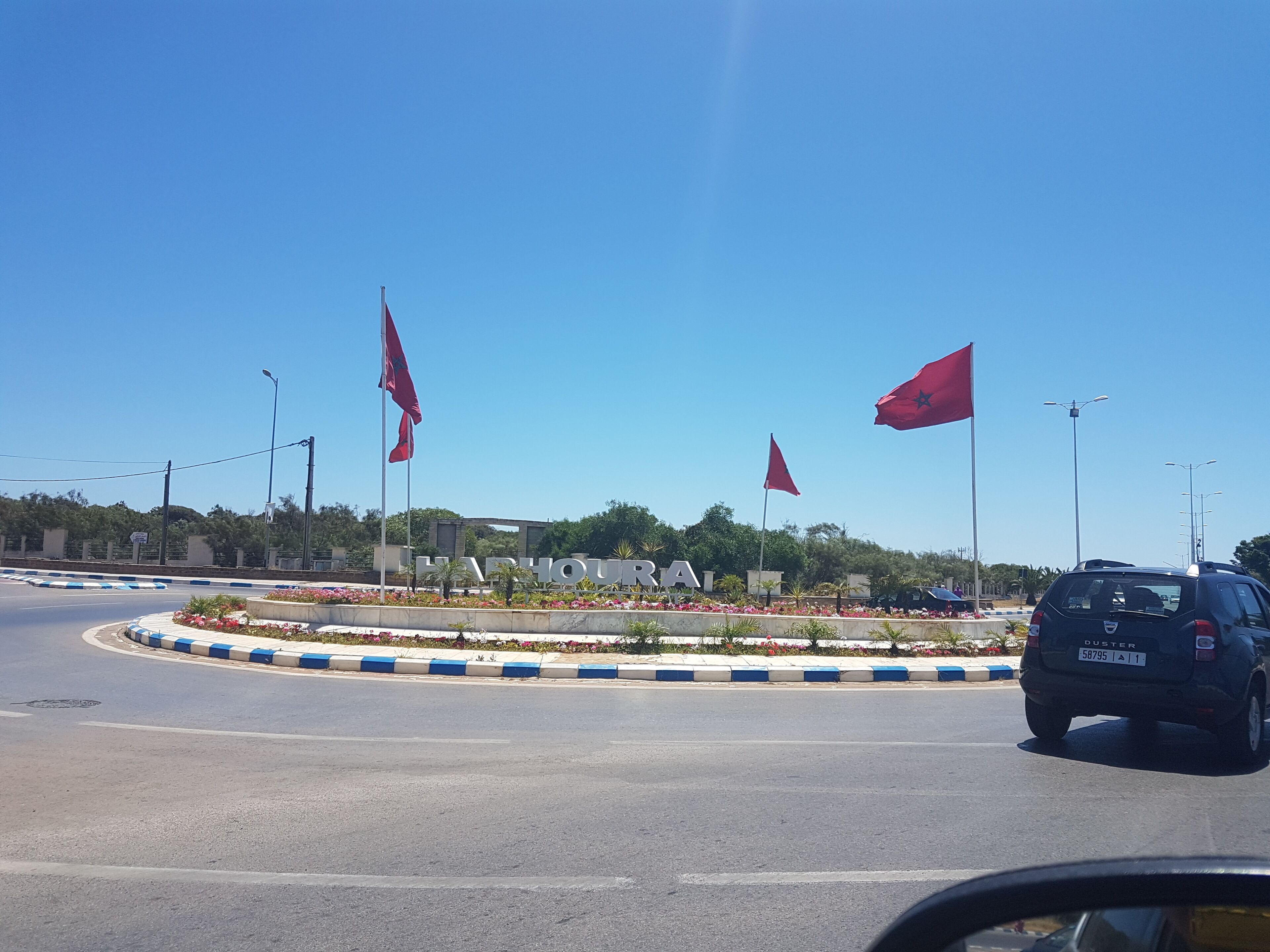 A roundabout with flags, a road, and a building with 'HARBOUR' sign.