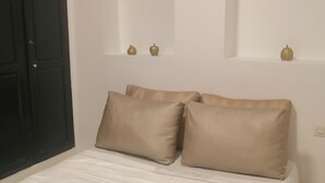 A bedroom with a bed, two pillows, a nightstand, and a wall-mounted shelf with decorative items.