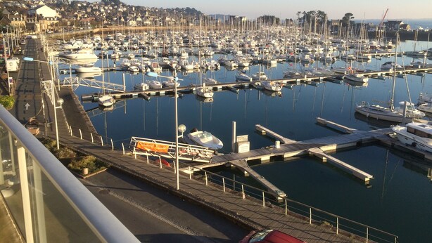A marina with numerous boats docked, a road with a red car, and a distant town. -  ENEZ BREHAT, Residence LE PORT, marina, Your balcony on the Port, (Perros-Guirec)