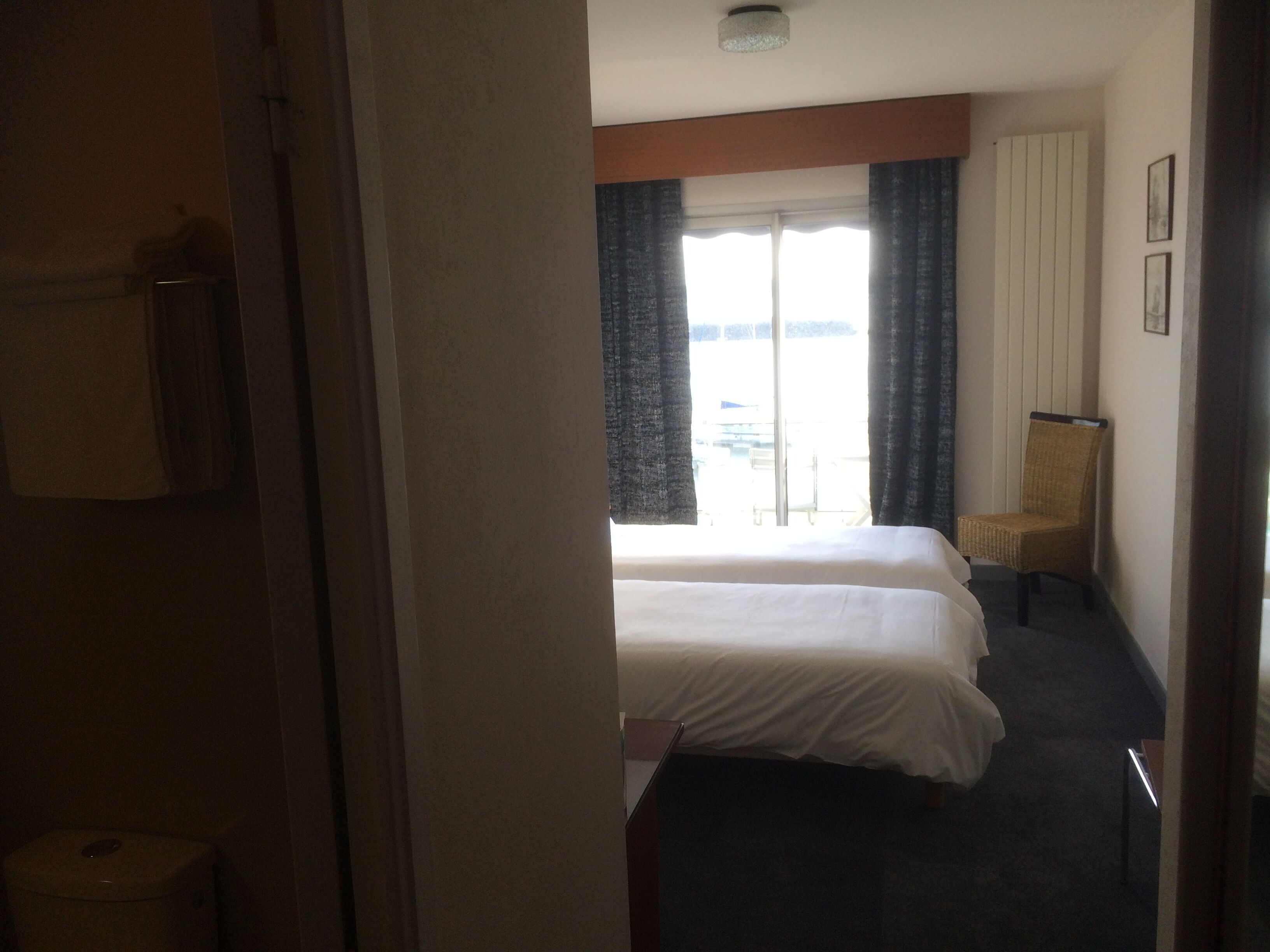 Une chambre d’hôtel avec deux lits, une chaise, une fenêtre avec des rideaux et une vue sur l’extérieur.