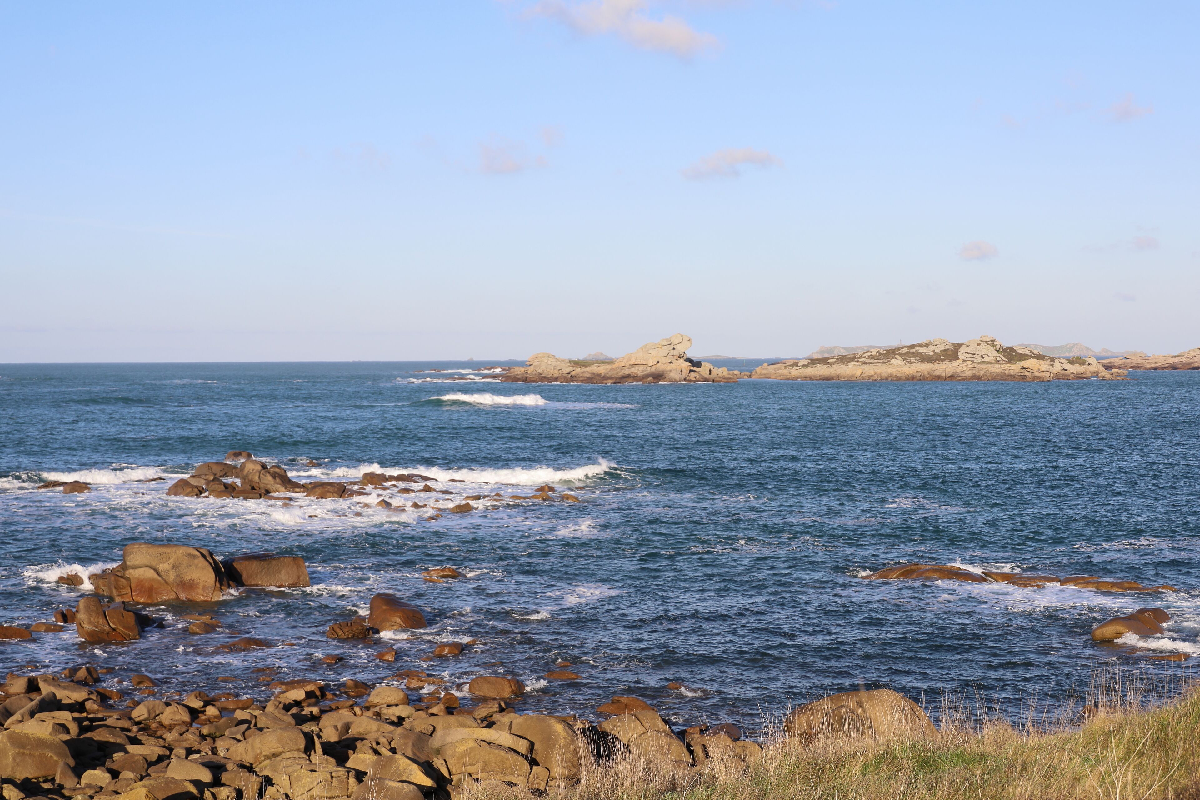 Una costa rocosa con olas rompiendo contra las rocas y una vista despejada de islas lejanas.