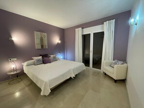 Een slaapkamer met een bed, een stoel, een nachtkastje en een schuifdeur die leidt naar een balkon.
