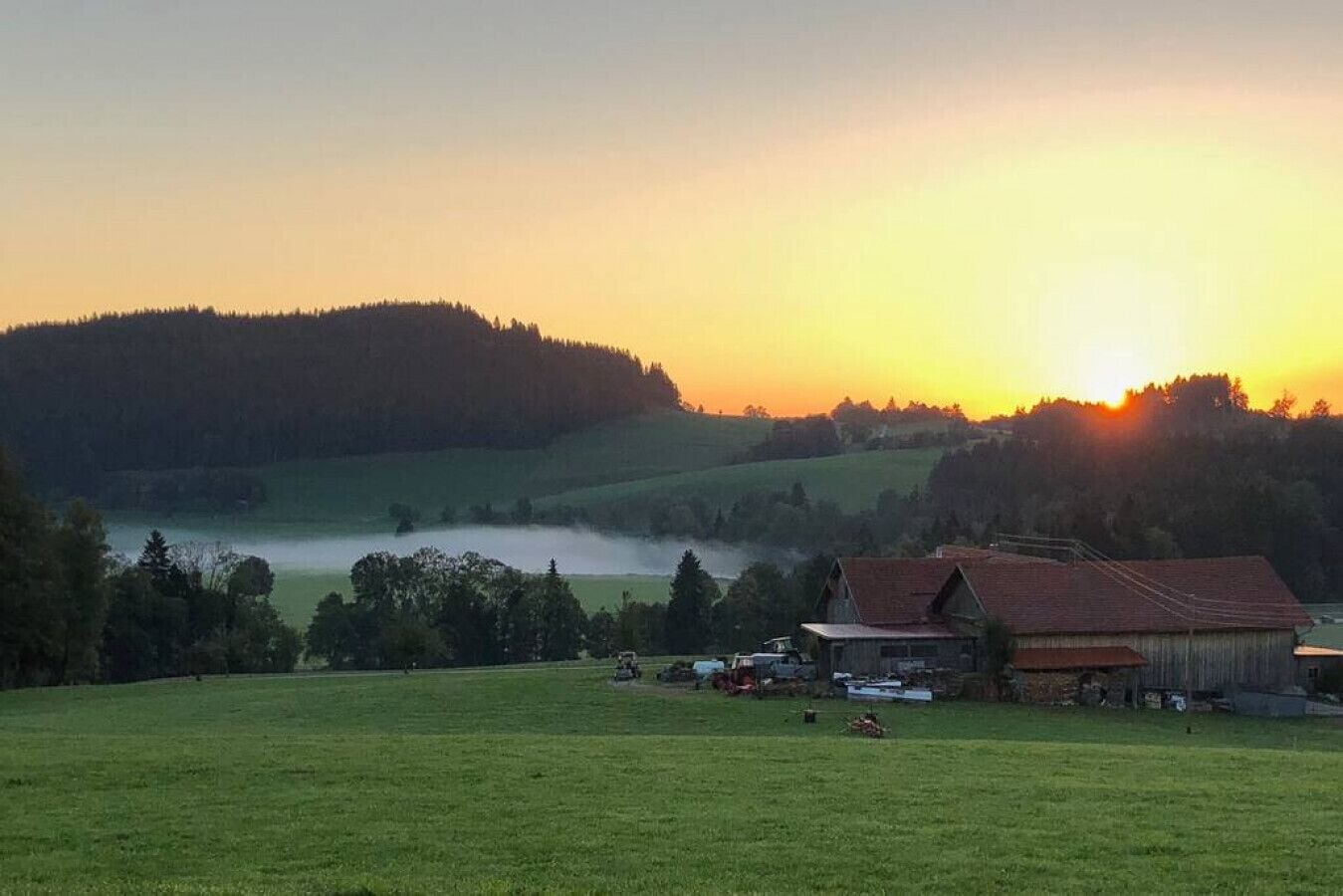 A rural landscape with a barn and open fields at sunset.