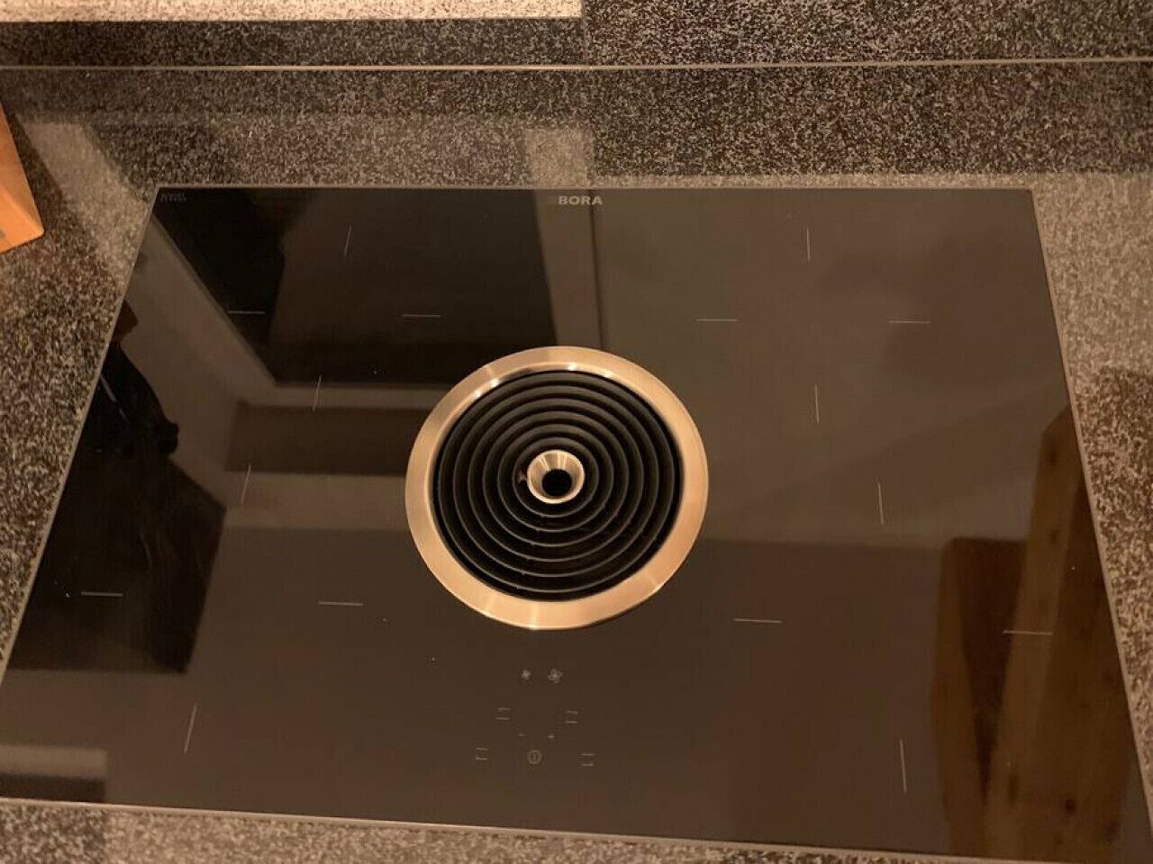 A black induction cooktop with a circular vent in the center, placed on a granite countertop.