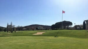 Ein Golfplatz mit Fahne, Sandbunkern und Häusern im Hintergrund.