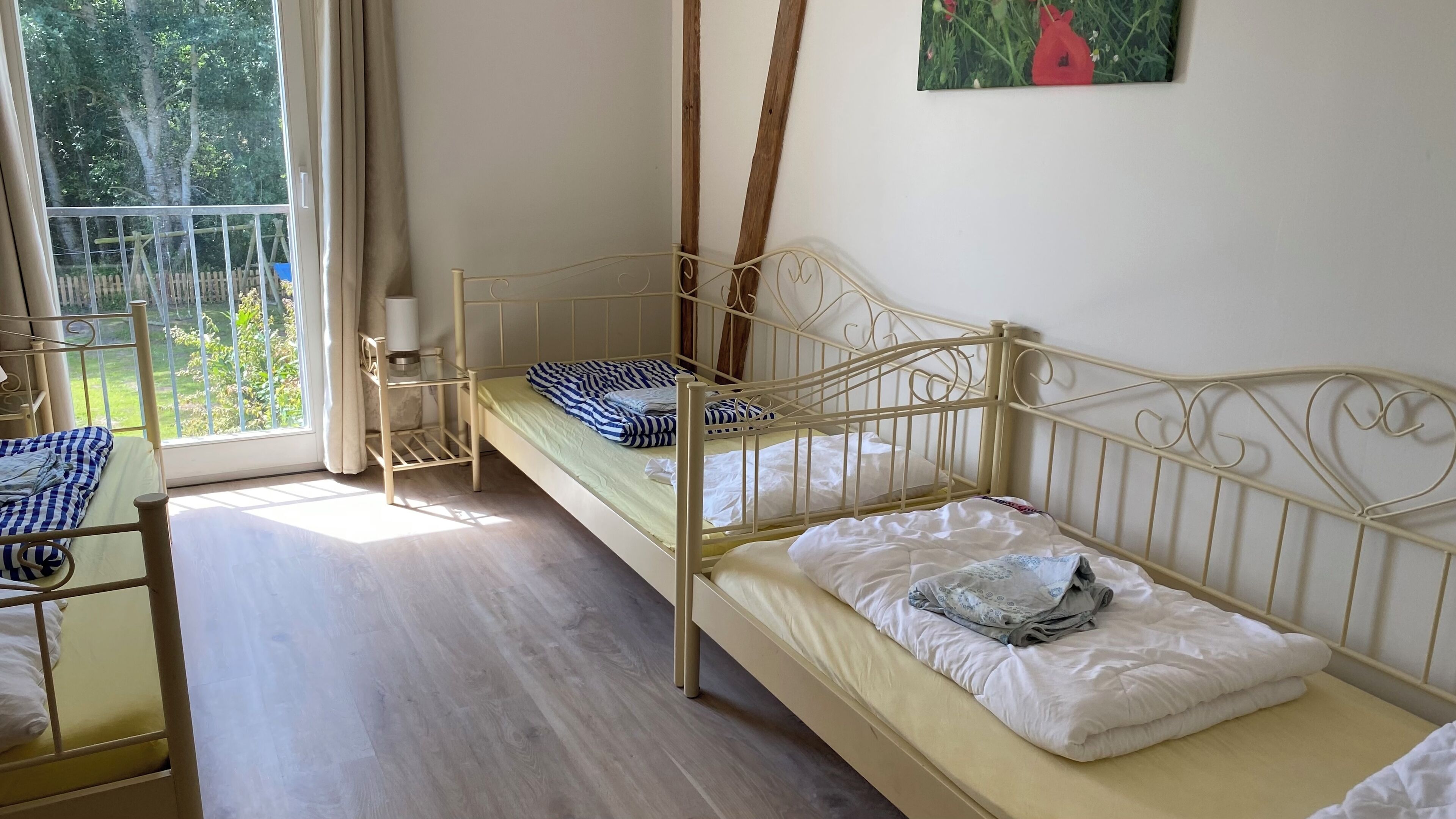 Ein Zimmer mit zwei Etagenbetten, einem kleinen Tisch mit Lampe und einem Fenster mit Blick auf Grünflächen.