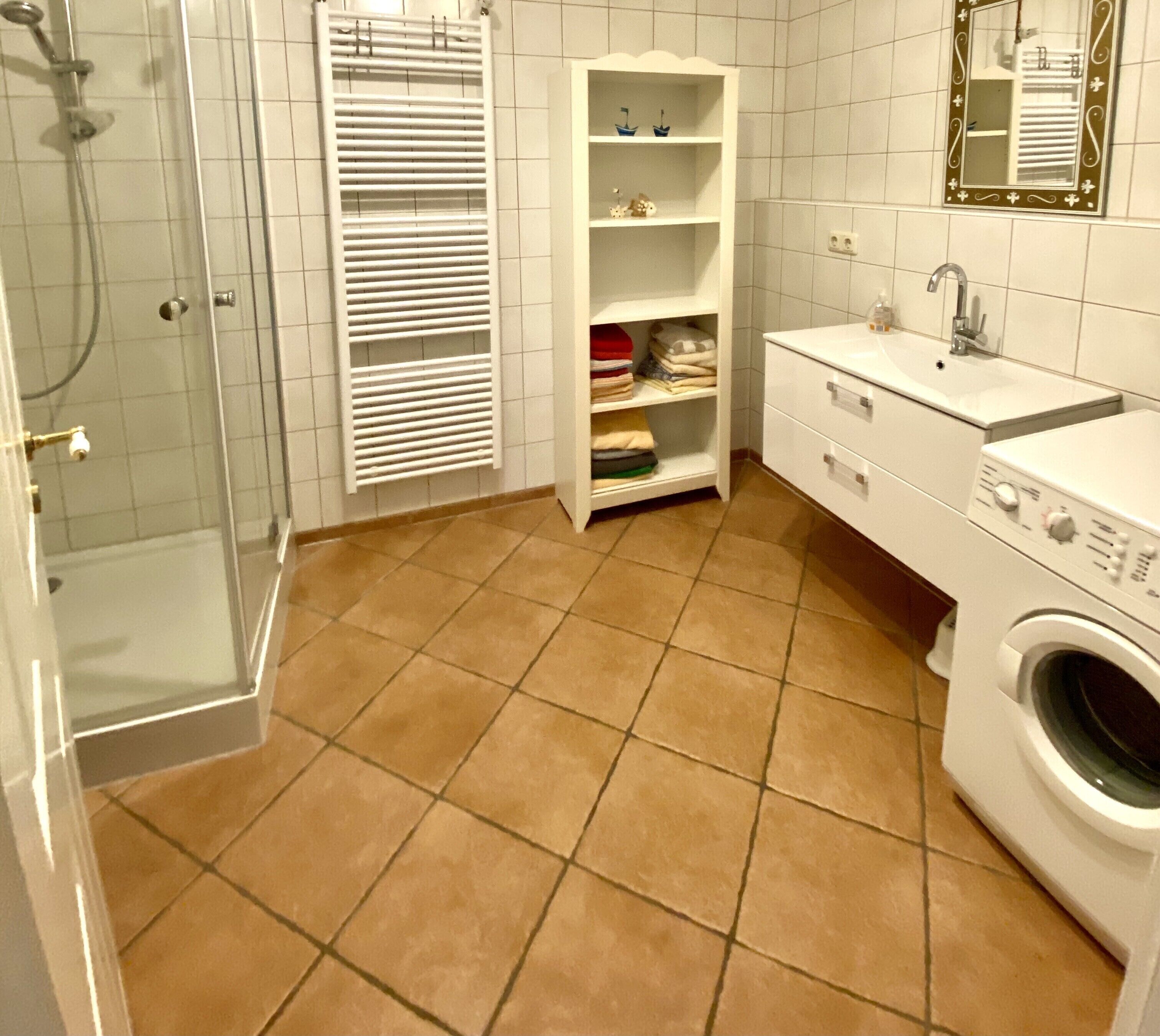 Een badkamer met een douche, een inbouwkast met opgevouwen handdoeken, een wastafel en een wasmachine.