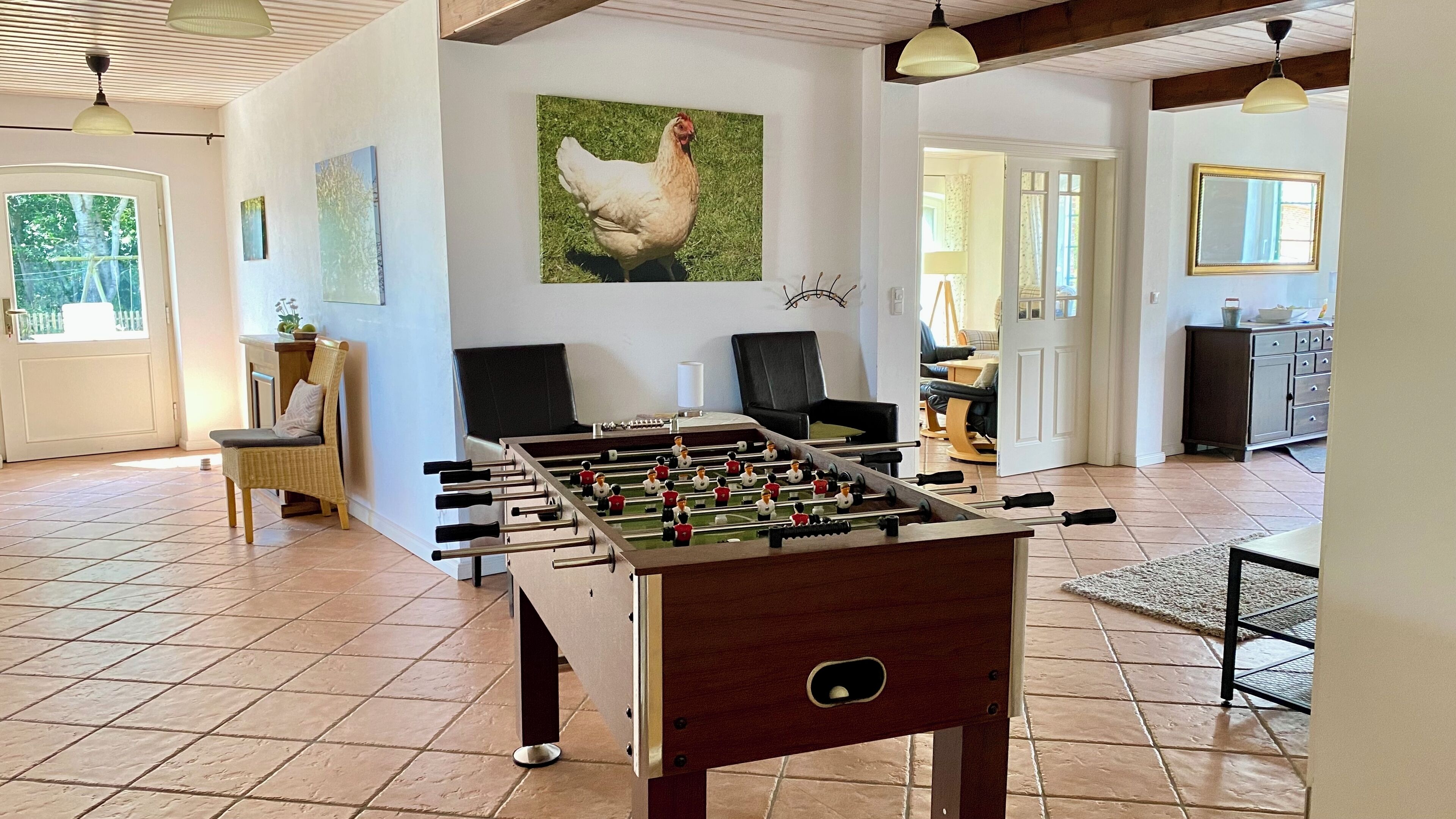 A room with a foosball table, a painting of a chicken, and a dining area with a table and chairs.